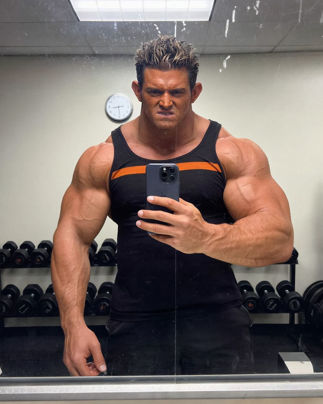 Elon Muskle taking a gym mirror selfie in front of a dumbbell rack